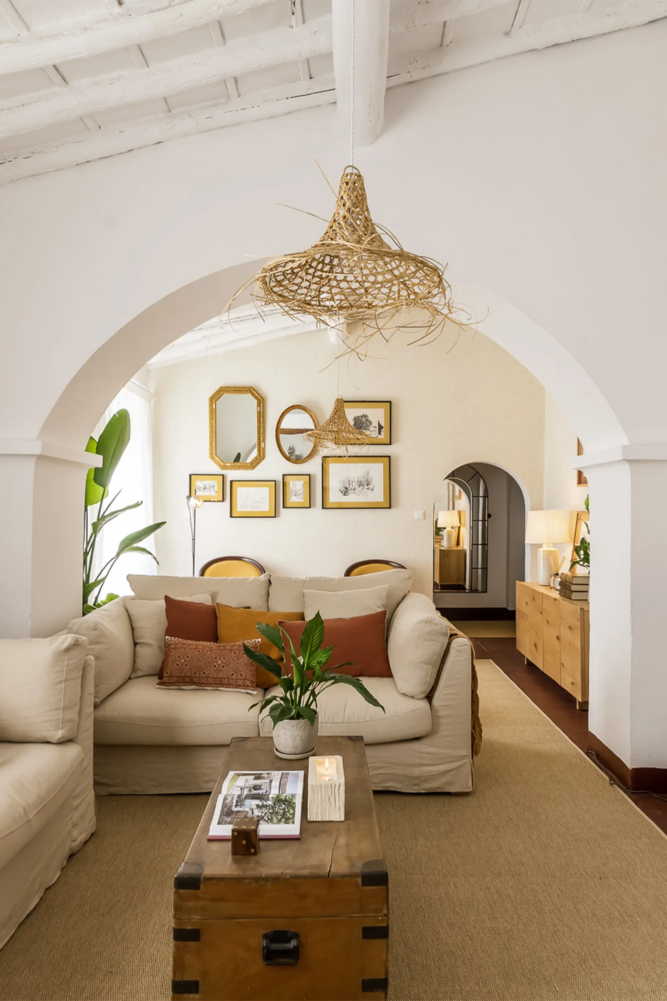 Sala de estar com passagem em arco, sofás claros e molduras agrupadas na parede.